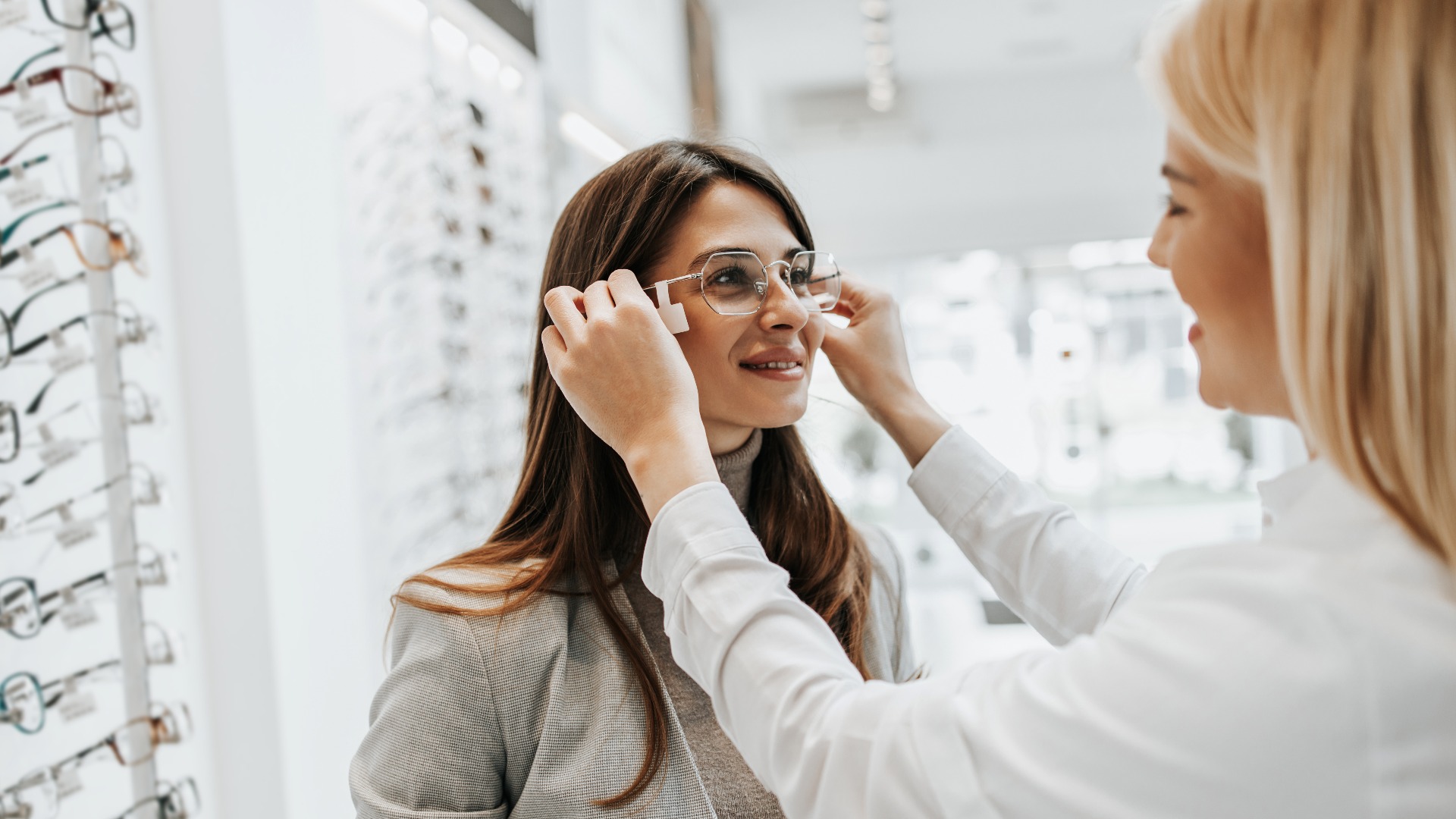 Frau sucht Brillengestell in Optikergeschäft, Verkäuferin hilft