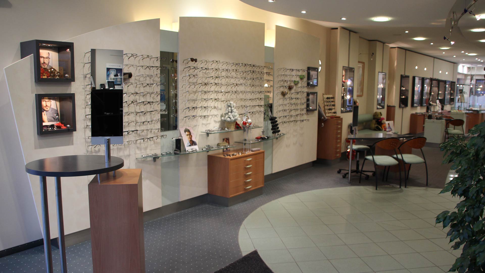 Ein moderner Optikerladen mit Brillenregalen und Werbefotos. Neutralfarben und hell beleuchtet.